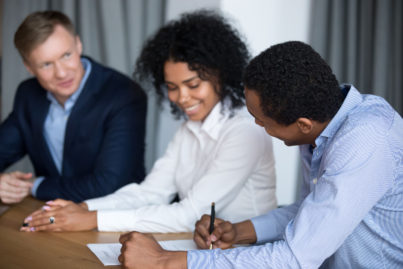 Smiling black man negotiate with diverse business partners sign cooperation deal at briefing, excited multiethnic businesspeople close deal put signature on agreement after successful meeting